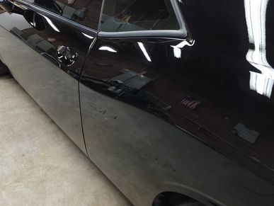 Close-up of a shiny black car door reflecting the surroundings.