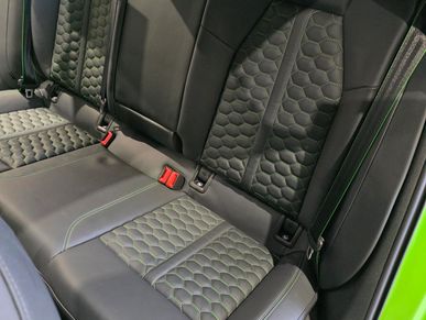 Rear seats of a car with black leather and honeycomb pattern upholstery.