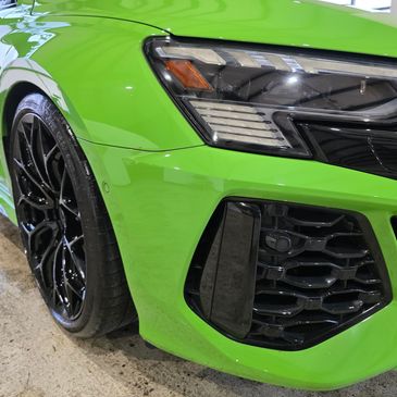 Close-up of a green sports car's front headlight and black wheel.