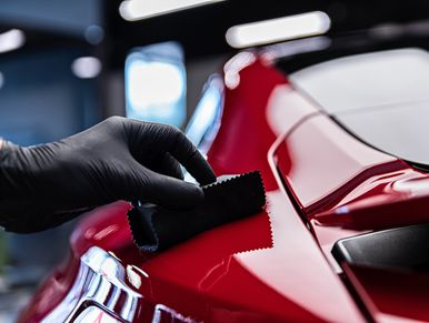 Hand polishing the red surface of a car with a cloth.