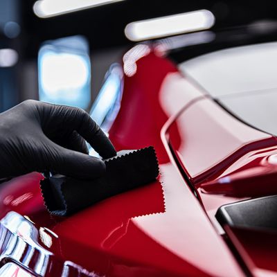 Hand polishing a shiny red car surface with a black cloth.