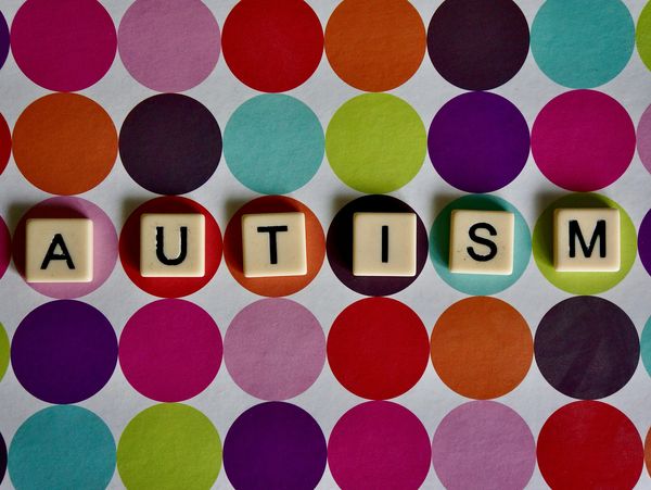 Blocks spelling 'AUTISM' on colorful polka dot background.