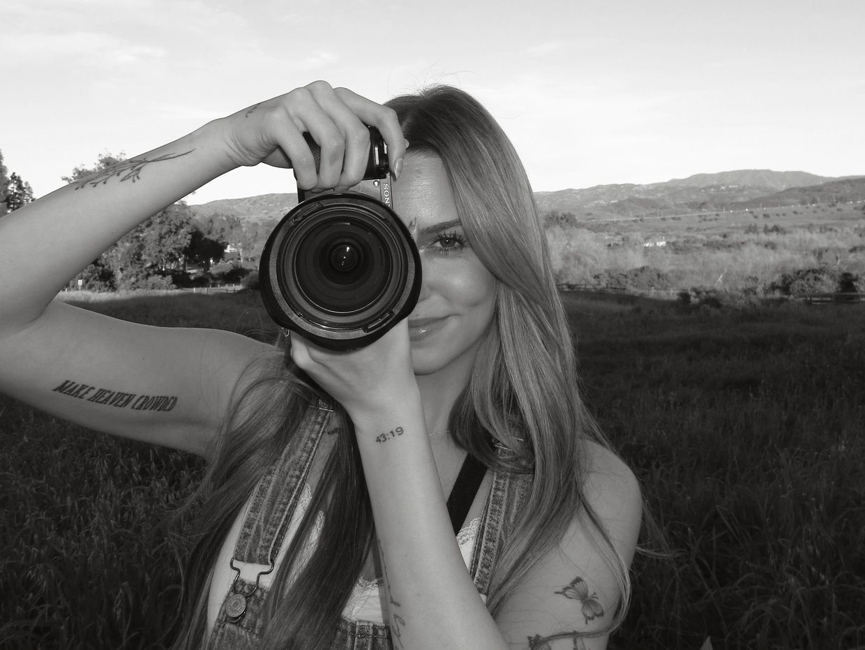 Young woman with tattoos taking a photo in a scenic outdoor setting.