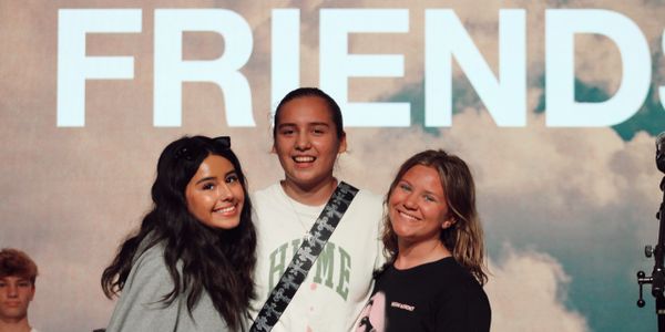 Three friends smiling in front of a FRIENDS sign.