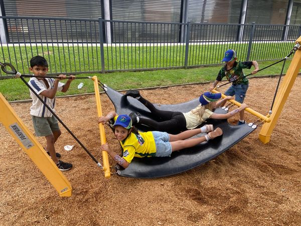 Four children playing on a large swing at a playground.