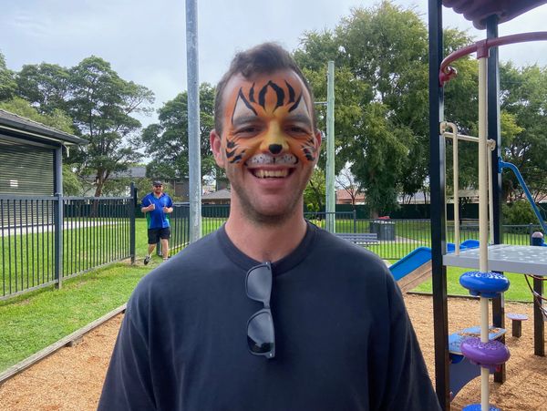 Man with tiger face paint smiling at a playground.