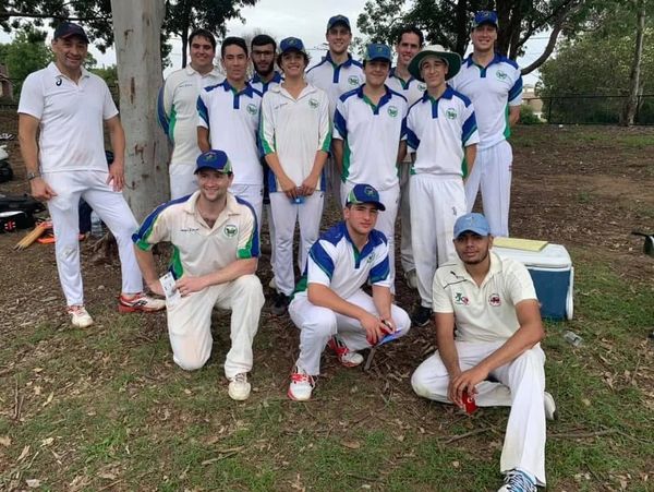 Cricket team posing outdoors in uniforms on a grassy field.