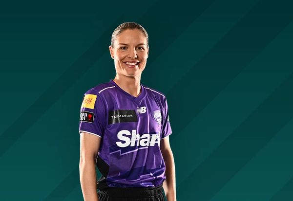 Smiling female athlete in a purple sports jersey against a teal background.