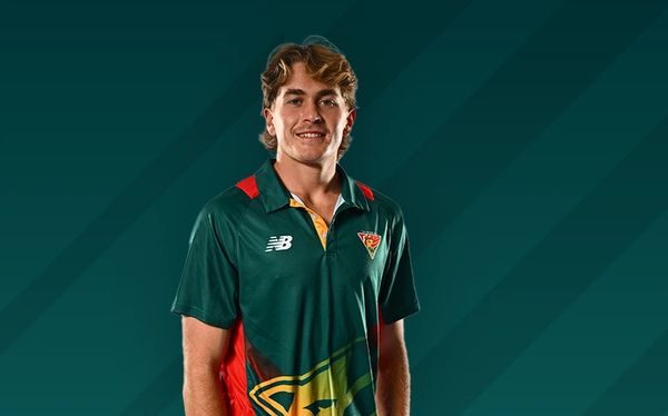 Young man in a sports jersey posing against a dark green background.