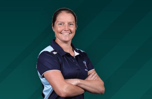 Confident woman in a sports polo shirt smiling with arms crossed against a teal background.