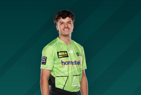 Cricket player in green uniform posing with a smile.