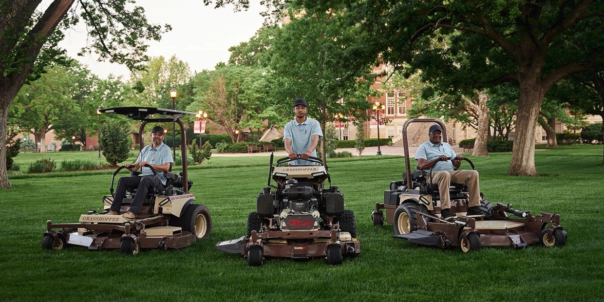 Three men on riding lawn mowers in a park-like setting.
