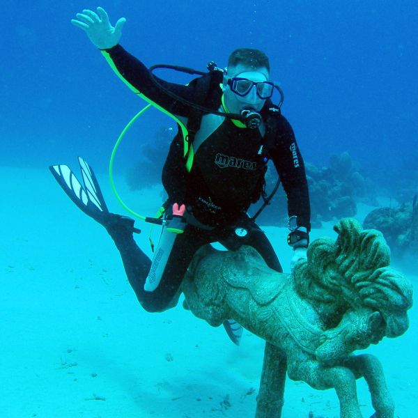 Diver poses underwater with a carved stone sculpture resembling a mythical creature.