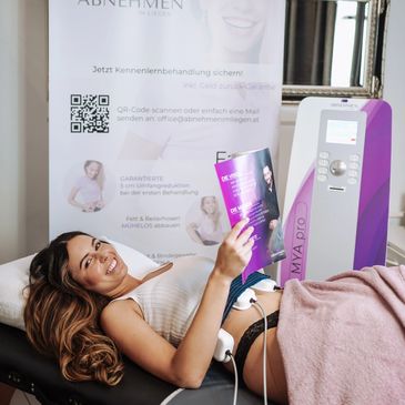 Smiling woman undergoing a body contouring treatment while reading a magazine.