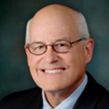 Smiling elderly man with glasses in a suit.