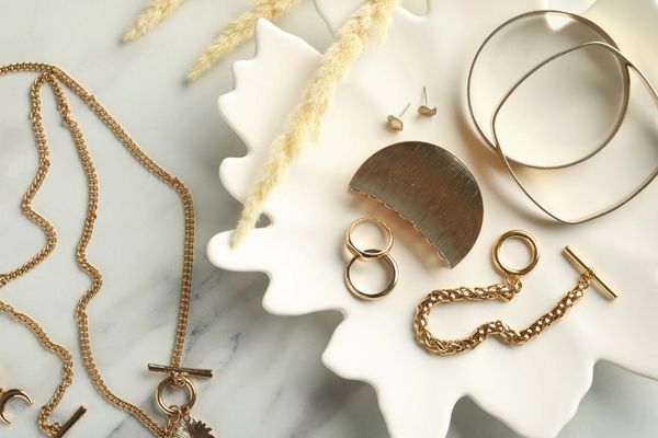 Assorted gold jewelry pieces displayed on a white decorative tray with a marble background.