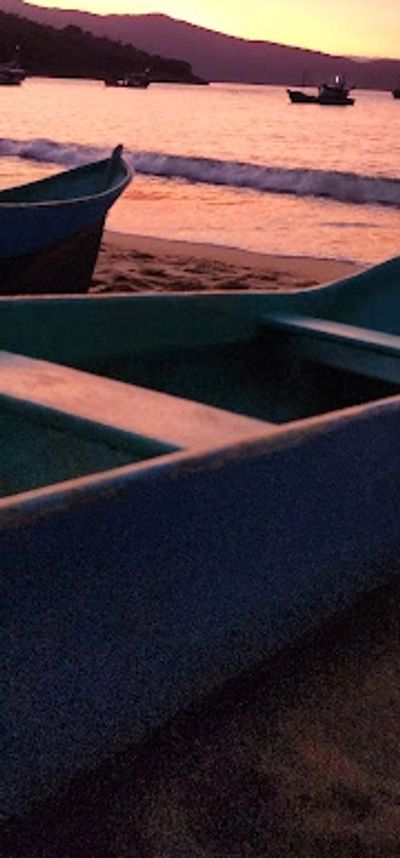 Boats resting on a beach during a serene sunset over calm waters.