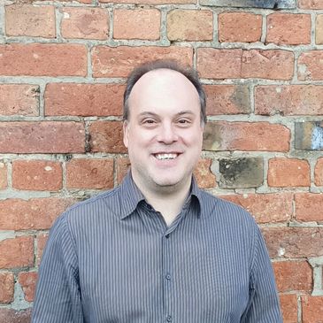 Photo of the smiling company director, Stefanos Apostolou, against a brick wall (Nottingham).