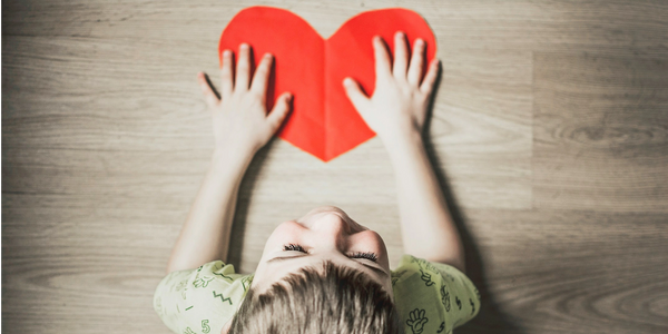 a child smiling and being thankful holding a red heart