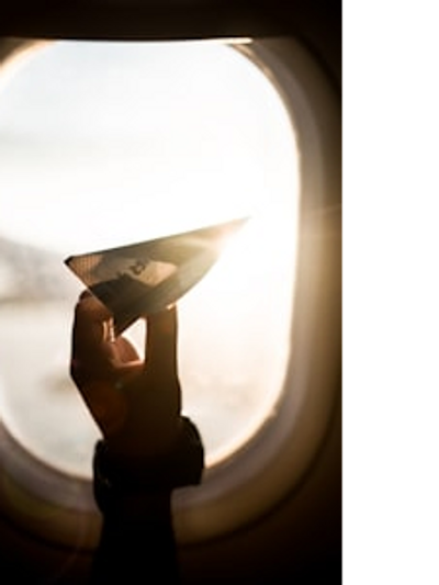 Youth travel and experiencing adventures and looking out airplane window holding a paper airplane