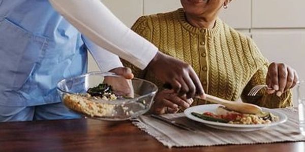 Person serving food to an elderly woman.