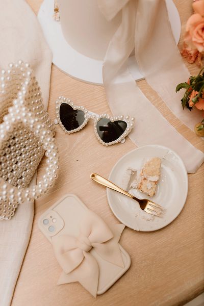 Lychee rose cake slice on a plate with gold fork surrounded by pearl and bow wedding accessories 