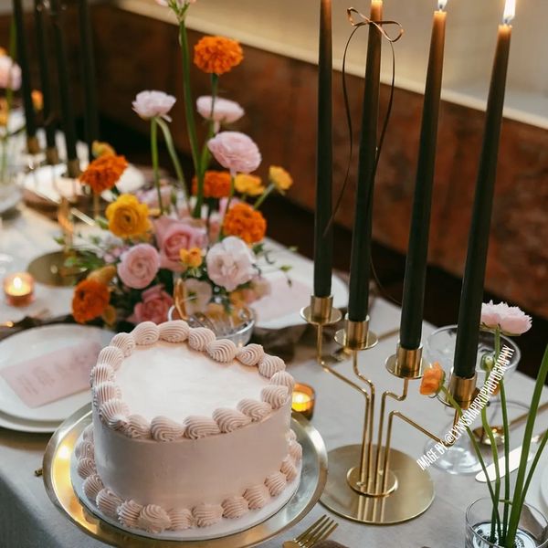 Pastel pink one tier lambeth cake on gold cake stand surrounded by colourful floral, bow and candles