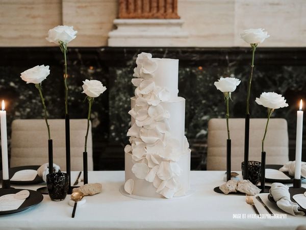 Modern rose petal cascade luxury 3-tier white wedding cake on table with roses and single stem vase