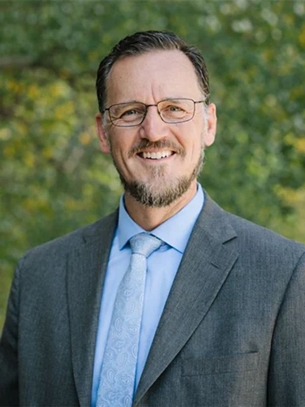 Smiling man in a suit and glasses outdoors.