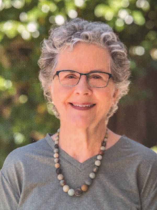 Smiling older woman with curly gray hair and glasses outdoors.