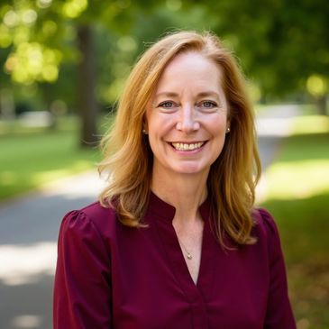 Smiling woman outdoors with green trees in background.