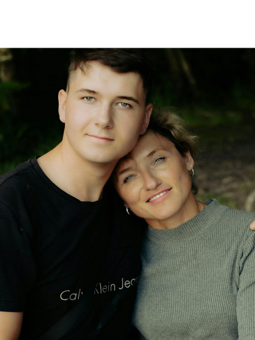 A young man and woman embracing outdoors, smiling gently.