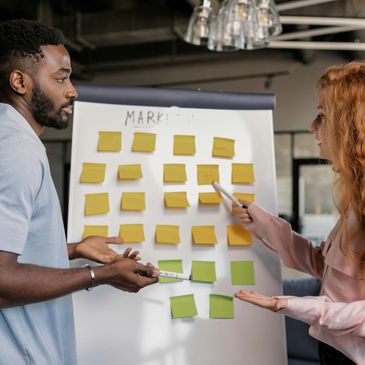Two colleagues discussing marketing ideas on a board with sticky notes.
