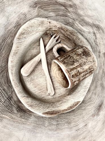 Rustic wooden cup, fork, knife, and plate on a textured wooden surface.