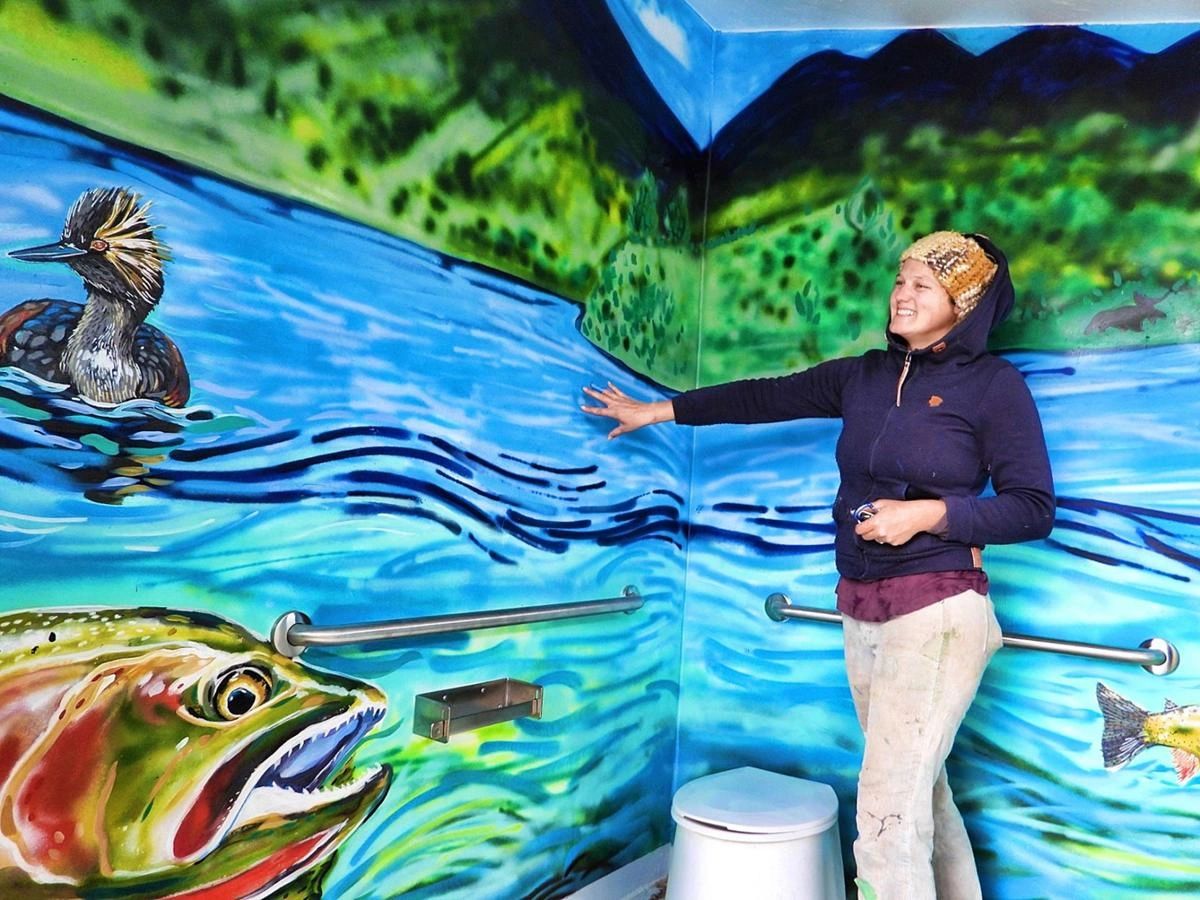 Helen Seay stands next to a mural she painted on the walls of a Bureau of Land Management vault toilet on the south side of Henry's Lake. | Courtesy of Bruce Hallman, Bureau of Land Management
