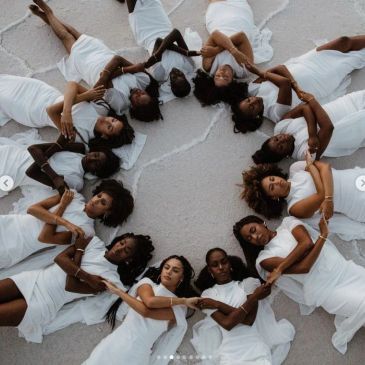 Women in white dresses lying in a circle holding hands.