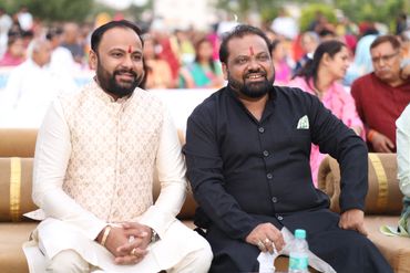 Two men in traditional Indian attire sitting and smiling at an outdoor event.