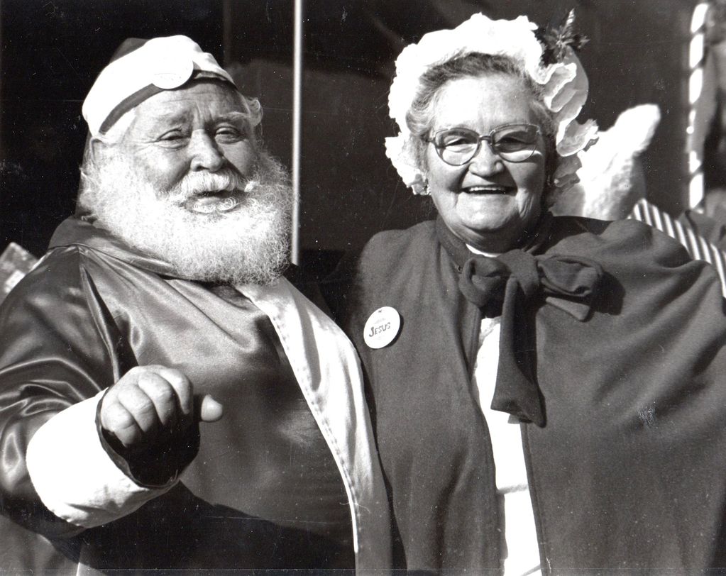 An elderly couple dressed in festive costumes, smiling warmly at the camera.