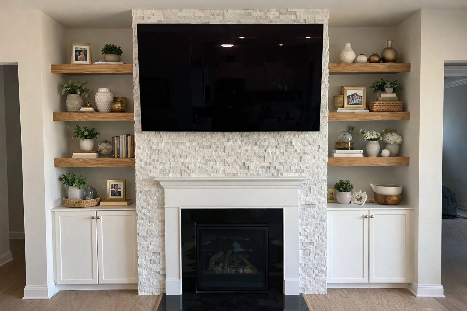 Modern white fireplace with TV and wooden shelves decorated with plants and vases.