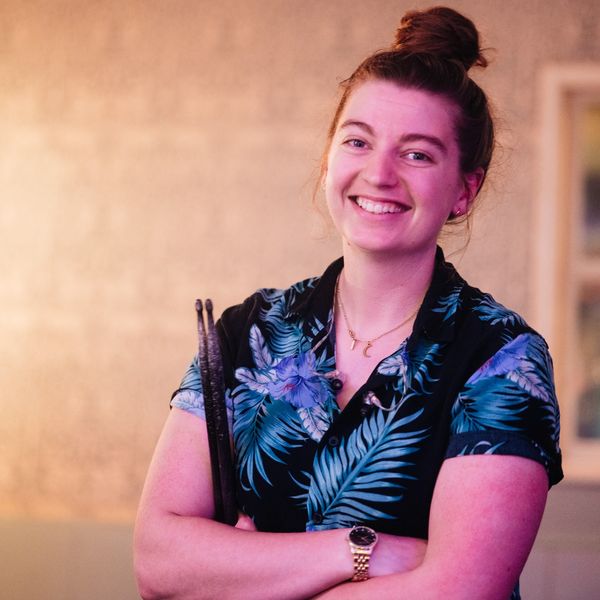 Woman smiling with drumsticks, wearing floral shirt.