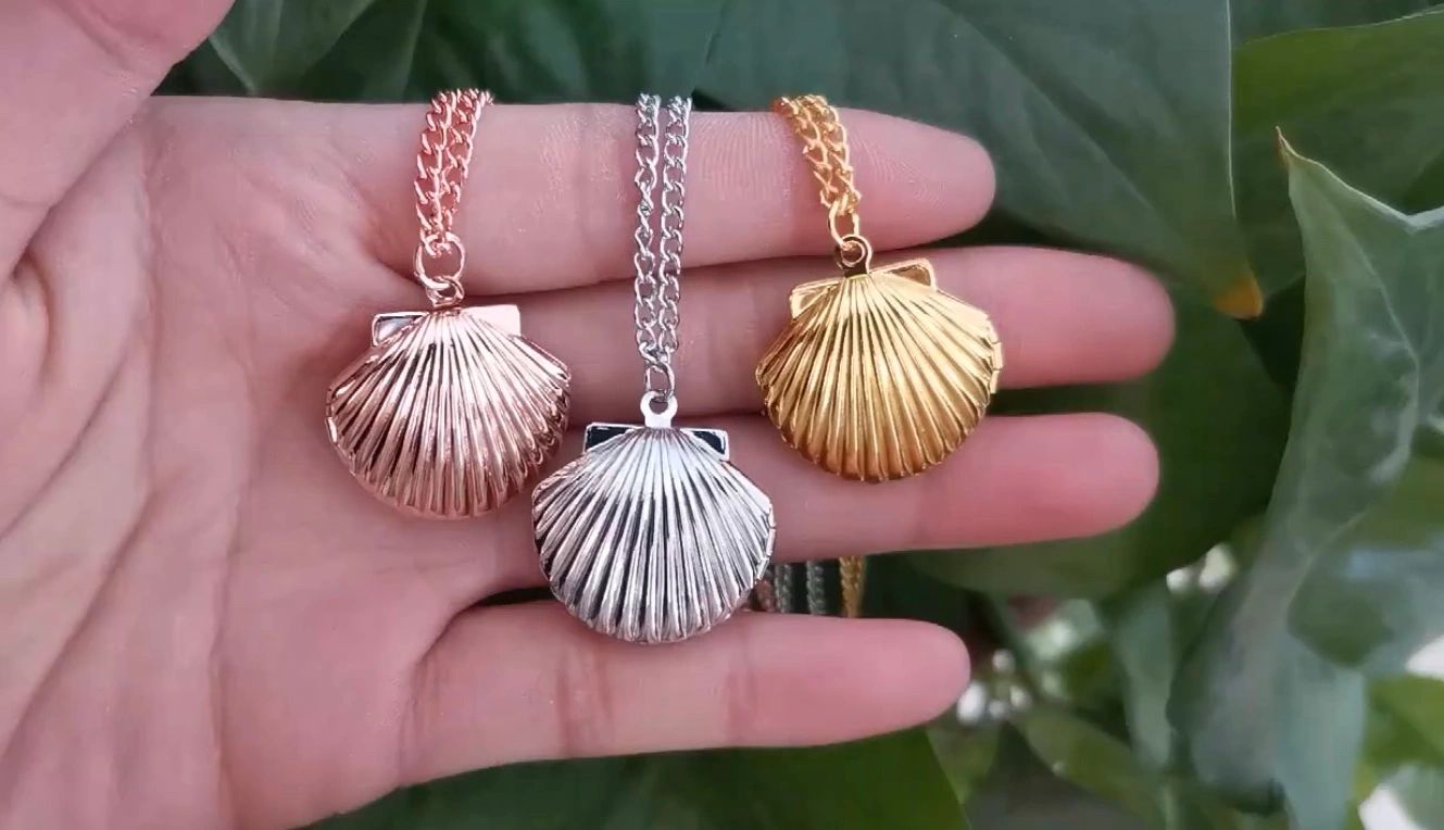 Hand holding three shell-shaped pendant necklaces in rose gold, silver, and gold.