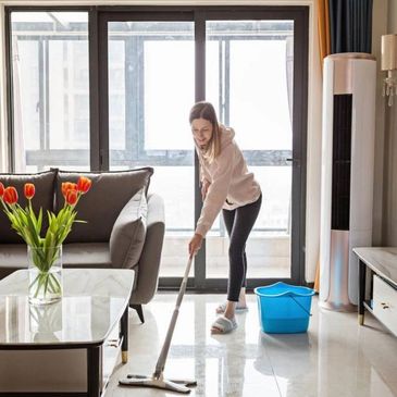 A woman mopping the floor in a bright living room.