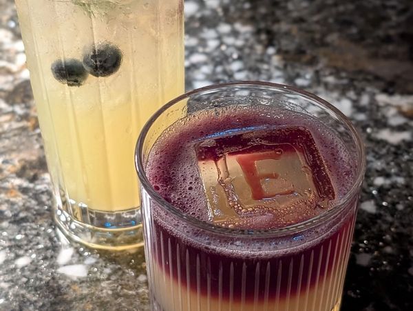 A blueberry lemon cocktail in a tall glass and a whisky sour with red wine float in rocks glass.