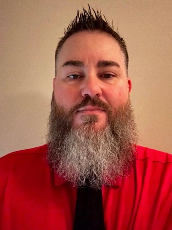 Man with a long gray beard wearing a red shirt.