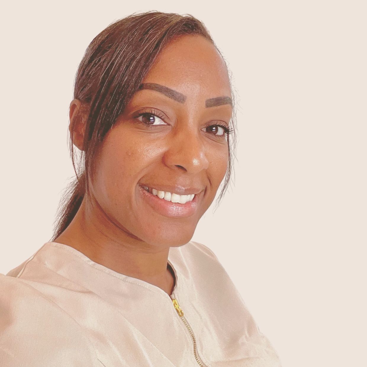 Smiling woman in a beige top with a zipper, against a plain background.