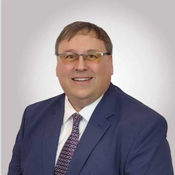 Smiling man in suit and glasses against a plain background.