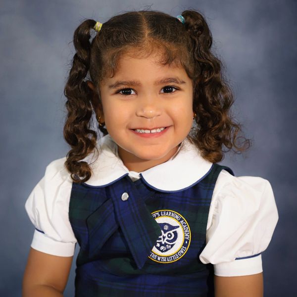 Smiling young girl in school uniform with curly pigtails.