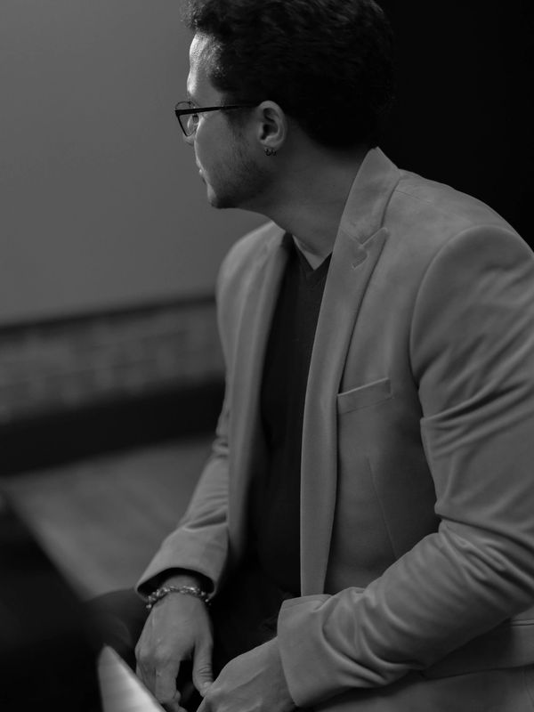 EdgarOnTheBeat sitting on a piano wearing a jacket in black and white