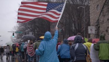 Person waves an American flag during a rainy outdoor event.