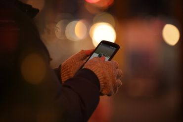 Person wearing gloves using a smartphone outdoors at night.